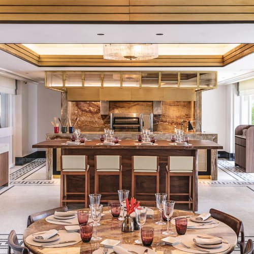 Elegant restaurant interior with a large round table set for dining and a bar area in the background, featuring modern decor and natural light.