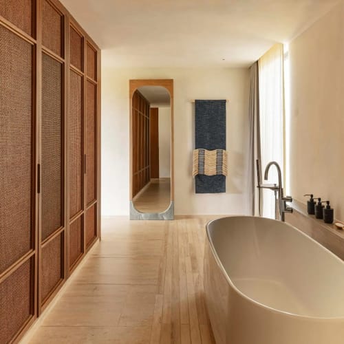 Modernes Badezimmer mit freistehender Badewanne neben einem großen Fenster mit Holzjalousien und einem an der Wand montierten Handtuchhalter mit blauen und beigen Handtüchern neben einem hohen Spiegel, der Holztürenschrank spiegelt.