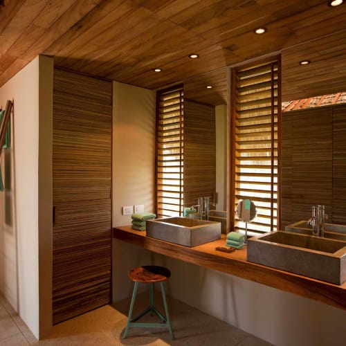 Moderne Badezimmer mit zwei quadratischen Waschbecken, Holzarbeitsplatte, großen Spiegeln und schmalen vertikalen Fenstern mit Holzjalousien, mit Holzschemel und einer Leiter mit Handtüchern.