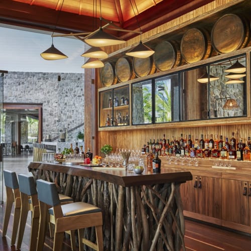 Whisky-Verkostung in einer rustikalen Bar mit Holzbarriken, Steinwänden und großen Fenstern, die natürliches Licht einlassen.