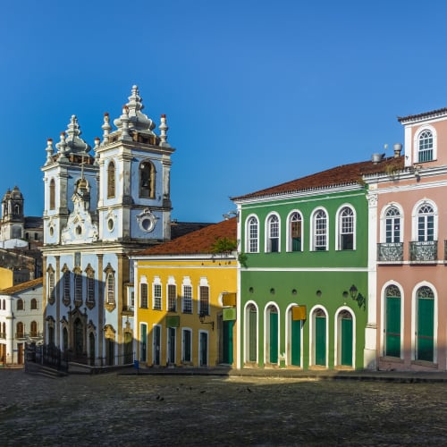 Bunte Kolonialgebäude und eine historische Kirche entlang einer Kopfsteinpflasterstraße in Pelourinho, Salvador da Bahia, Brasilien.