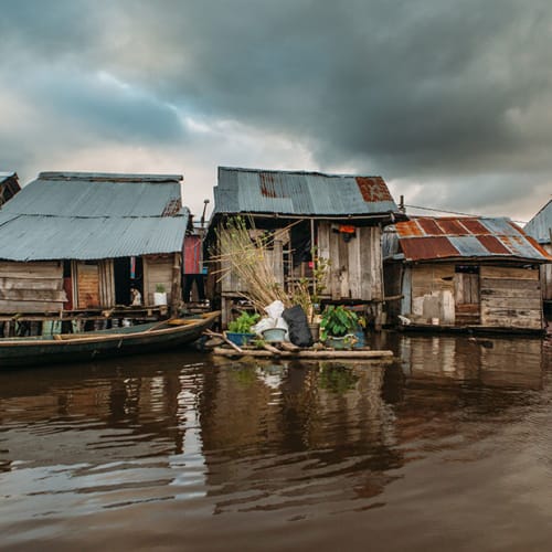 Eine Ansammlung von Holzhaus auf Stelzen über Wasser unter dunklem, bewölktem Himmel.