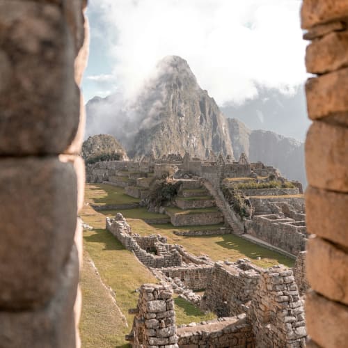 View of Machu Picchu through a stone window with mountain in the background.