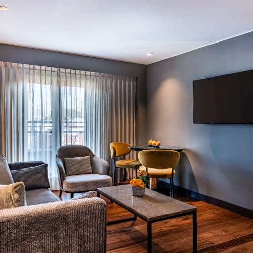Ein modernes Lounge-Bereich mit Sofa, Sessel, Couchtisch und einem Fernseher an einer blauen Wand in einer Hotelwohnung.
