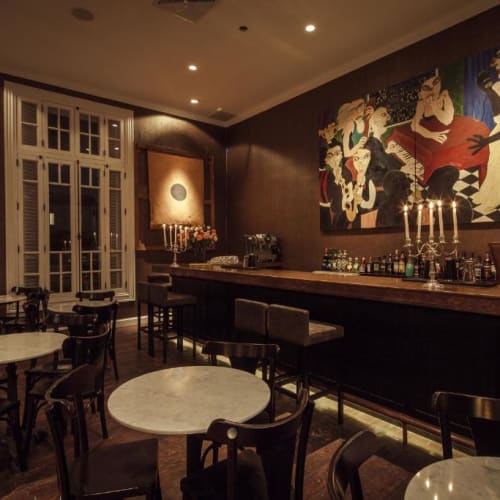 Eine gemütliche Hotelbar mit runden Marmor-Tischen, schwarzen Stühlen, warmer Beleuchtung und Kunstwerken an der Wand.