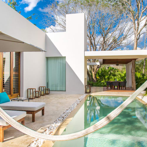 Moderner Außenbereich mit Liegestühlen, Sonnenschirm und Hängematte neben einem privaten Pool, umgeben von üppigem Grün und weißen Wänden.