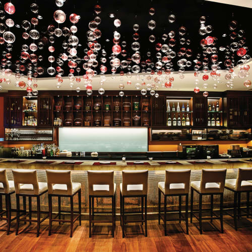 Elegante Bar mit einem geschwungenen Tresen und Barhockern, beleuchtet durch moderne Beleuchtung mit hängenden dekorativen Kugeln.