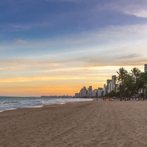 Ein ruhiger Strand bei Sonnenuntergang mit Hochhäusern und Palmen entlang der Küste