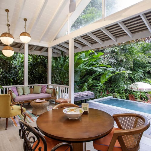 Überdachte Außen Terrasse mit Holztisch und gemischten Sitzgelegenheiten mit Blick auf einen privaten Pool, umgeben von üppigen tropischen Pflanzen.
