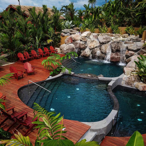 Ein üppiger tropischer Garten mit einem Schwimmbad, umgeben von roten Liegestühlen und Grünpflanzen in Costa Rica.
