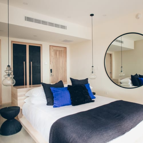 Modernes Hotelzimmer mit einem großen Doppelbett, schwarzen und blauen Kissen, einem runden Spiegel und minimalistischer Dekoration.