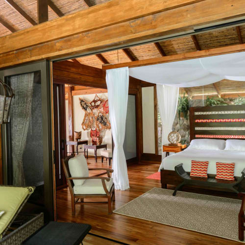 Luxuriöses Schlafzimmer mit Himmelbett, Holzmöbeln und künstlerischer Wanddekoration in einer tropischen Lodge.