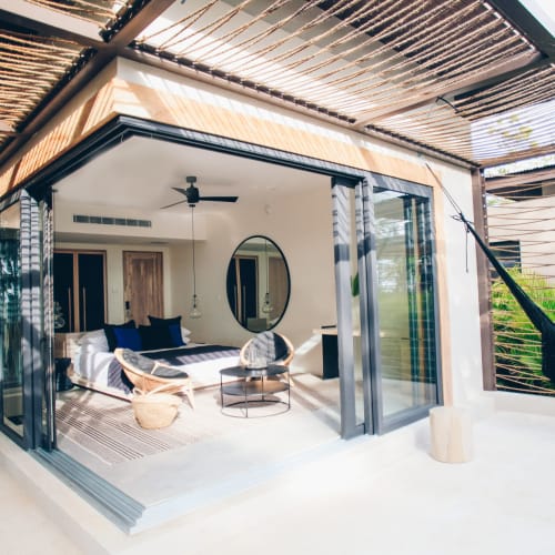 Ein gemütliches Schlafzimmer mit modernem Design, offen zu einem Außenbalkon mit Hängematte, umgeben von Grün.
