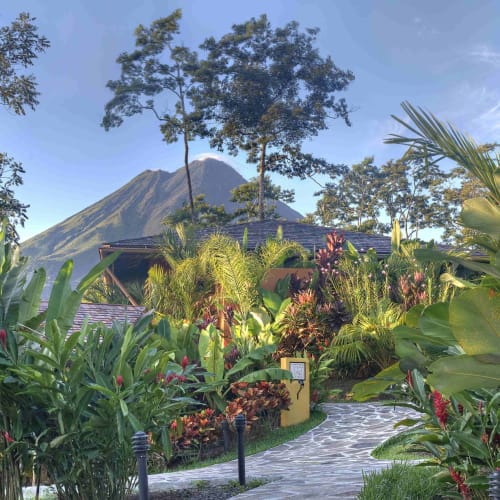 Üppiger tropischer Garten mit einem Weg, der zum Nayara Springs Resort führt, mit einem Vulkan im Hintergrund.