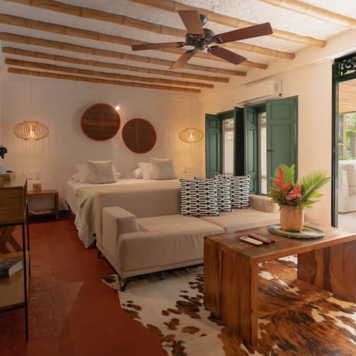 Eine gemütliche Suite mit großem Bett, Sofa, Couchtisch und offenem Balkon mit Grünpflanzen.
