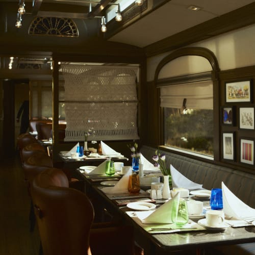 Luxuriöser Speisewagen des Andean Explorer Zuges mit Tischen, die mit weißen Servietten, Glaswaren und Ledersesseln gedeckt sind, beleuchtet von natürlichem Licht durch große Fenster.