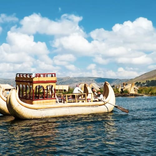 Traditional reed boats floating on Lake Titicaca near Puno, Peru, with mountains and partly cloudy sky in the background.