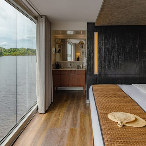 A luxurious river cruise cabin with a large window overlooking a lush green landscape and water.