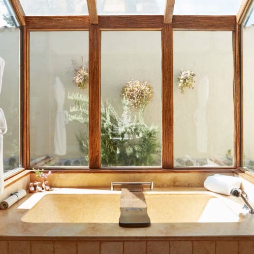 Ein gemütliches Badezimmer mit Badewanne vor einem großen Fenster mit Milchglas und Blumen Dekorationen.
