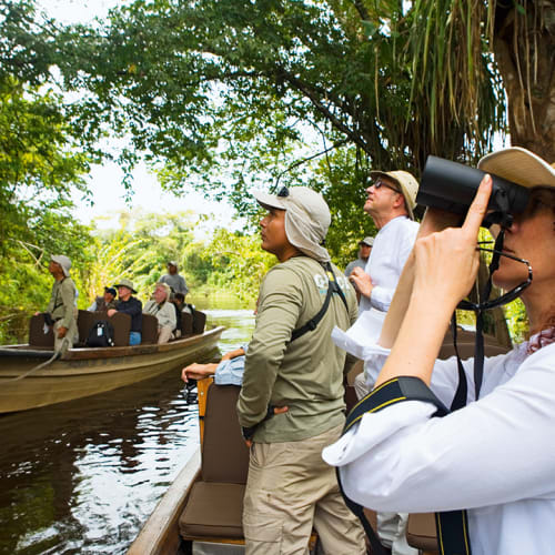 Gruppe von Touristen auf einem Boot im Amazonas-Regenwald, beobachtend Wildlife durch Ferngläser und Kameras.