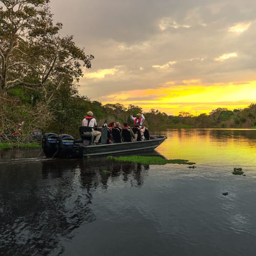 Eine Gruppe von Menschen auf einem Boot, die während des Sonnenuntergangs in einer üppigen, grünen Landschaft einen Fluss erkunden.