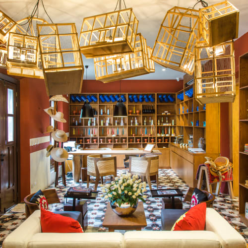 Innenraum eines gemütlichen Ladens mit Holzböden und Regalen voller Flaschen, einem zentralen Sitzbereich mit weißen Sofas und roten Kissen sowie einzigartigen hängenden Holzkäfig-Laternen unter warmem Licht.