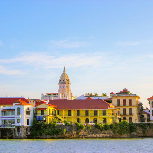 Colorful buildings along a river with a tall clock tower in the background under a blue sky.