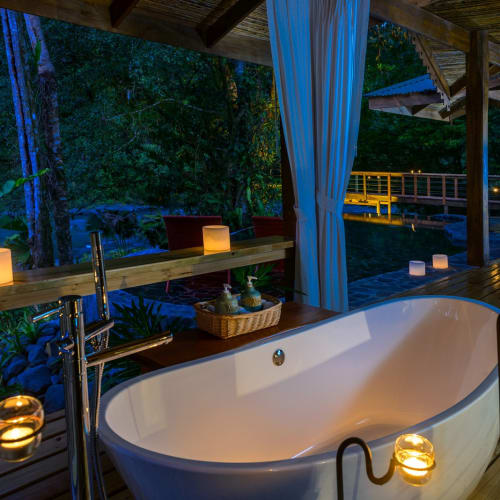 Eine luxuriöse Outdoor-Badewanne auf einer Veranda im Pacuare Lodge, umgeben von Kerzen und dichtem Regenwald.