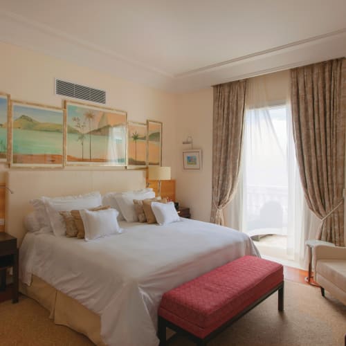 Luxuriöses Hotelzimmer mit großem Bett, dekorativen Bildern und Sitzbereich nahe einem Fenster mit Vorhängen.