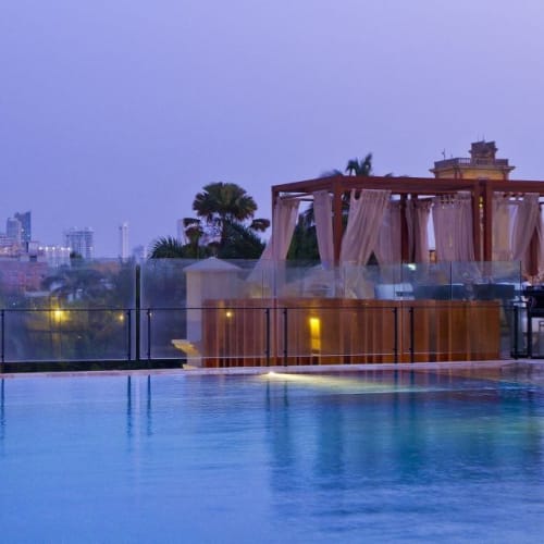 Ein luxuriöser Hotel-Dachpool mit Blick auf die Stadtskyline und einem beleuchteten Turm im Hintergrund bei Dämmerung.