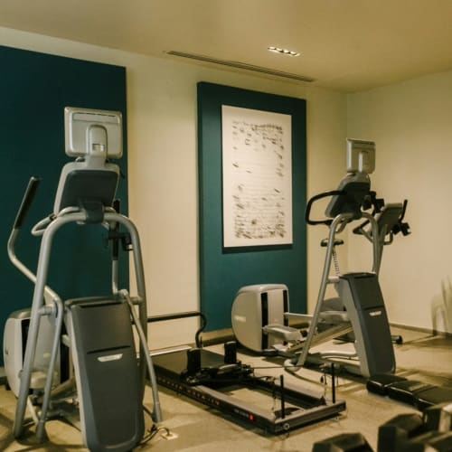Innenraum eines Fitnessstudios mit Trainingsgeräten wie Crosstrainern und einem Rudergerät, an der Wand hängt ein gerahmtes Bild in einem gut beleuchteten Raum.