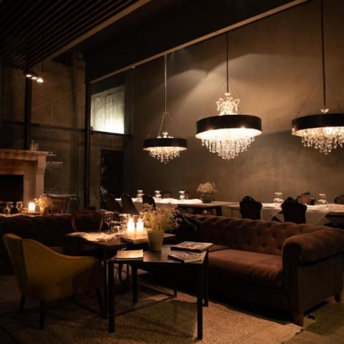 Elegant dining room with dim lighting, featuring chandeliers, sofas, and a fireplace.