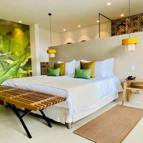 A modern hotel room with a large bed, decorative pillows, a bedside table, and artistic wall decor.