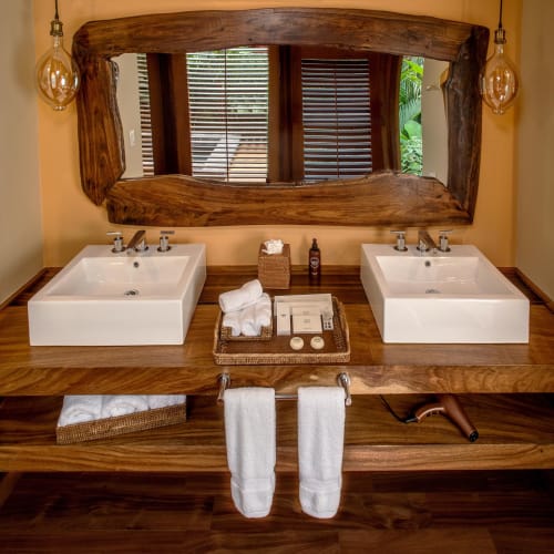 Double bathroom with two sinks, large wooden-framed mirror, and decorative lighting, set in a cozy room with wooden accents.