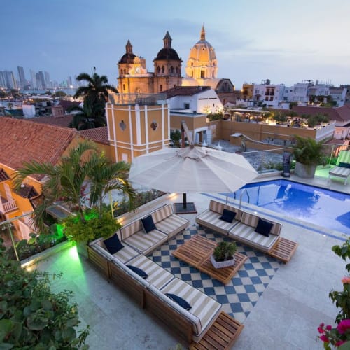 Dachterrasse bei Sonnenuntergang mit Liegen, Sonnenschirmen, einem Pool und historischen Gebäuden im Hintergrund in Cartagena de Indias.