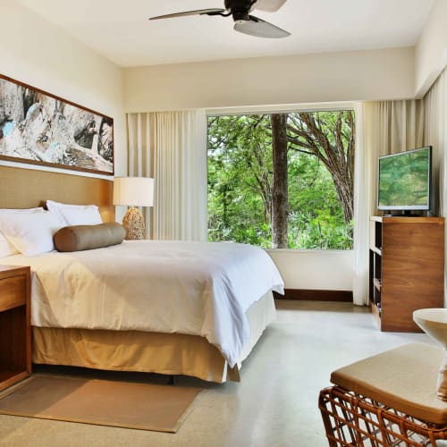 Elegantes Hotelzimmer mit großem Bett, Holzmöbeln und Blick auf grüne Bäume außerhalb des Fensters.