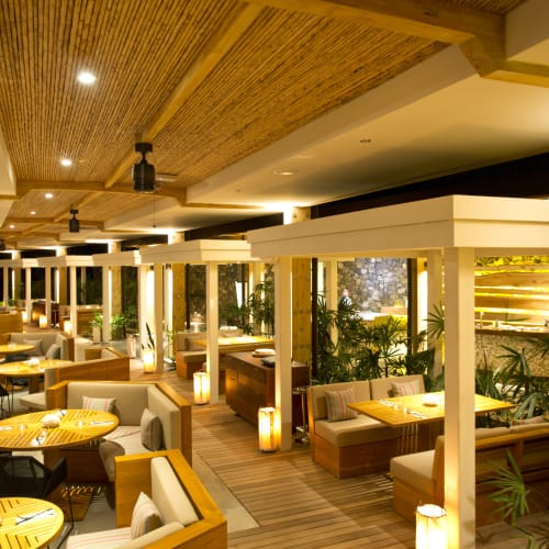 Ein Außenrestaurantbereich im Andaz Costa Rica Resort mit Holzkonstruktionen, gepolsterten Sitzgelegenheiten und warmem Licht inmitten tropischer Pflanzen.
