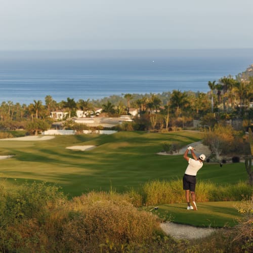 Golfer schlägt Abschlag auf dem One & Only Palmilla Golfplatz mit Meerblick und umgeben von Grünflächen und Palmen.