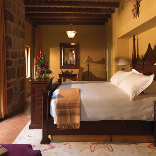 A cozy bedroom with a large bed, decorated with Christmas flowers, with a window showing a garden outside.