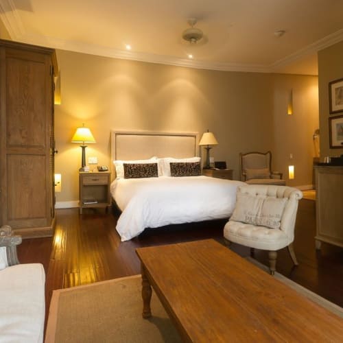 Elegant hotel room with a large bed, armchairs, wooden furniture, and warm lighting.