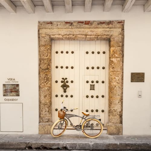 Ein altes, elegantes Fahrrad mit Korb vor einer alten, kunstvollen Holztür, umrahmt von Steinwerk in Cartagena, Kolumbien.