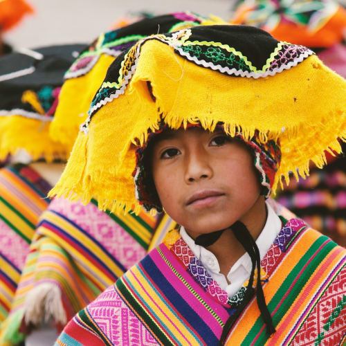 Young boy wearing colorful traditional Peruvian clothing and a bright yellow hat, participating in a cultural event in Cusco, Peru.