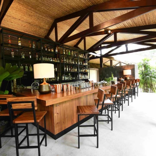 Ein stilvolles Bar-Innenraum im Tabacón Thermal Resort and Spa mit einer Holzbar, modernen Stühlen und einem großen Fenster, das natürliches Licht hereinlässt.
