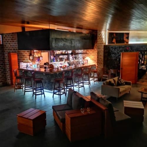 A dimly lit bar area with a brick wall background, a marble countertop, and seating including bar stools and a small sofa.