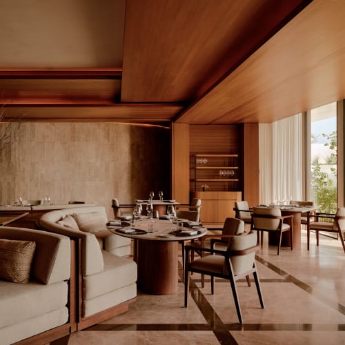 Moderner, eleganter Restaurantbereich mit beigen Polsterstühlen und Sofas, runden Holztischen mit Gläsern, weichem natürlichem Licht durch hohe Fenster mit transparenten Vorhängen und warmen Holzdetails in der Architektur.