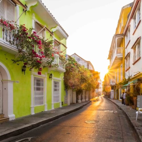 Sonnenuntergang, der einen warmen Schein über bunte koloniale Gebäude in einer ruhigen Straße in der Altstadt von Cartagena wirft.
