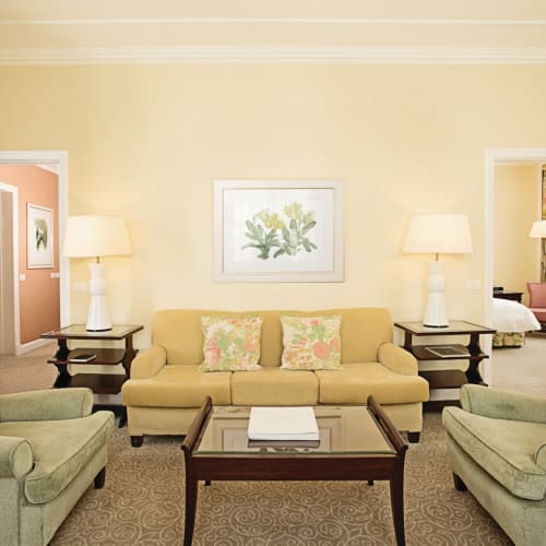 Elegant living room with two green armchairs, a beige sofa, and wooden coffee table in a luxurious suite.