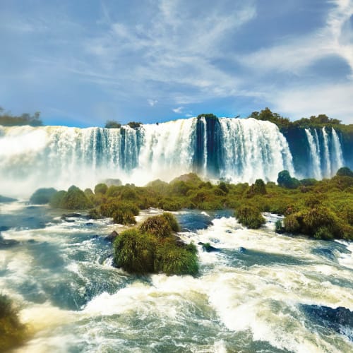 Die mächtigen Iguazu Fälle mit herabstürzendem Wasser inmitten üppigem Grün unter einem bewölkten Himmel.