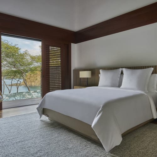 Luxuriöses Schlafzimmer mit großem Bett, Holzelementen und Blick auf Wasser und Bäume draußen.