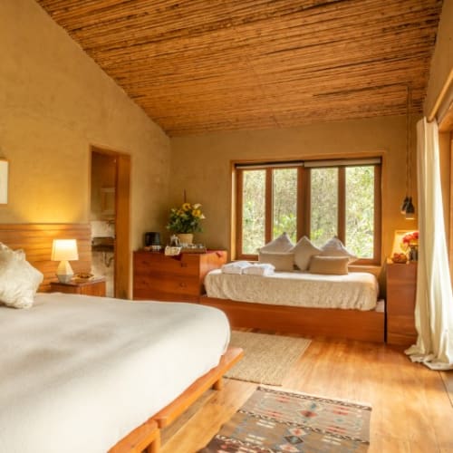 A cozy bedroom with a large bed, a sitting area by the window, wooden furniture, and a balcony with sliding doors.